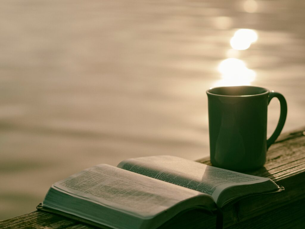 A warm cup of coffee and an open journal on a bench overlooking the sea at sunset — peaceful moment for reflecting and budgeting calmly.