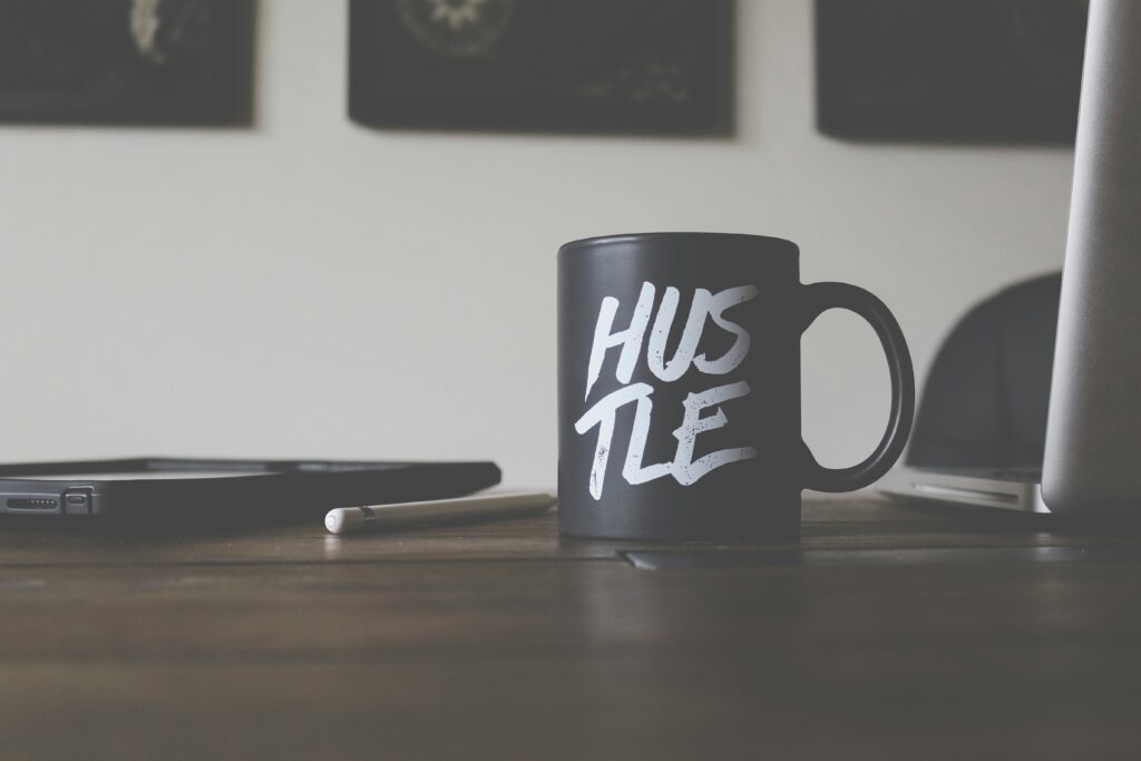 black ceramic coffee cup with the word “Hustle” printed on it, symbolizing motivation and side hustle energy during a personal savings challenge.