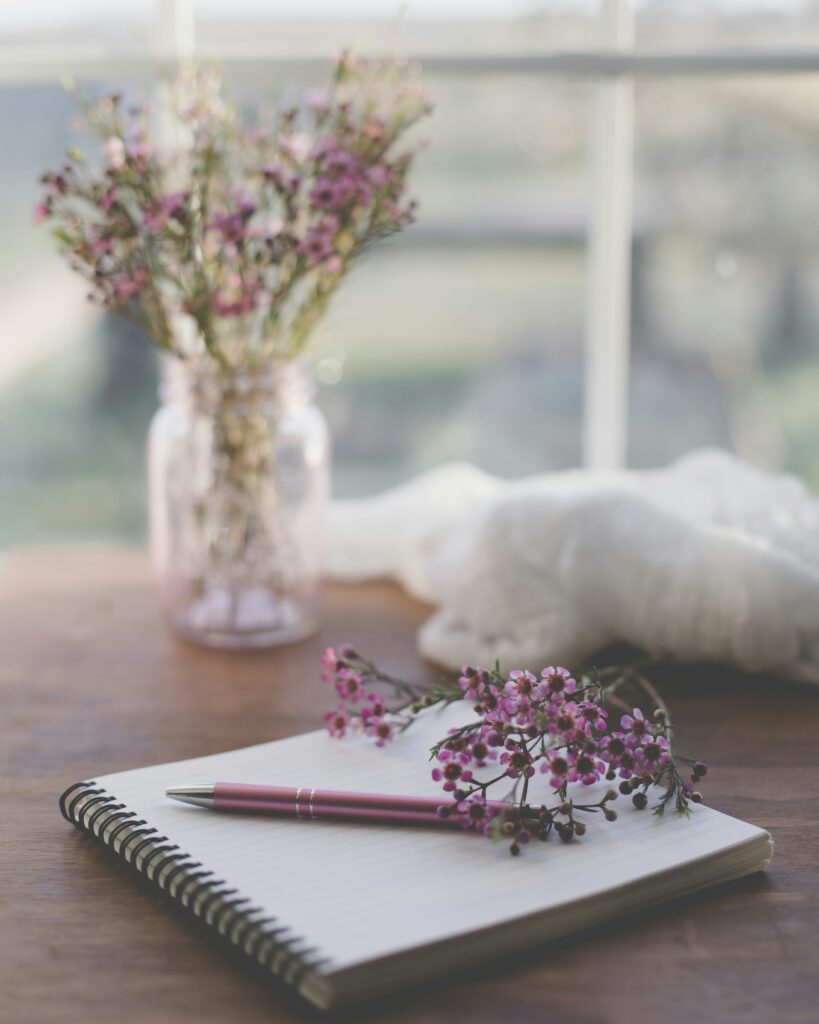Notebook and pen on a table with a purple flower, symbolizing calm and mindful money planning