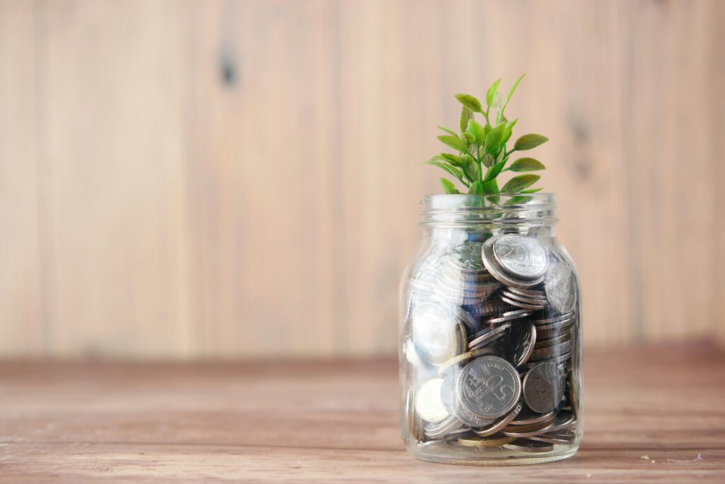 A glass jar filled with coins and a small green plant growing from the top, symbolizing saving money and financial growth.