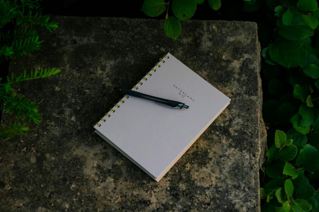 A simple notebook and pen resting on a stone surface outdoors, representing budgeting, financial planning, and a fresh money reset.